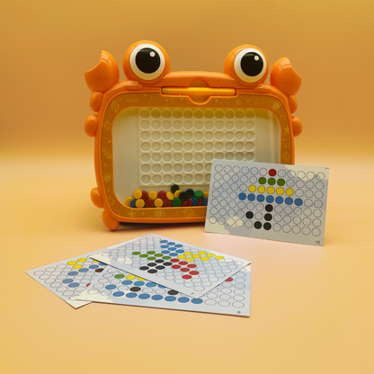 A children's toy color-sorting game set shaped like a cartoon crab, with an orange crab-shaped container holding small multicolored balls, plus several printed color-sorting cards placed in front on a warm beige studio background.